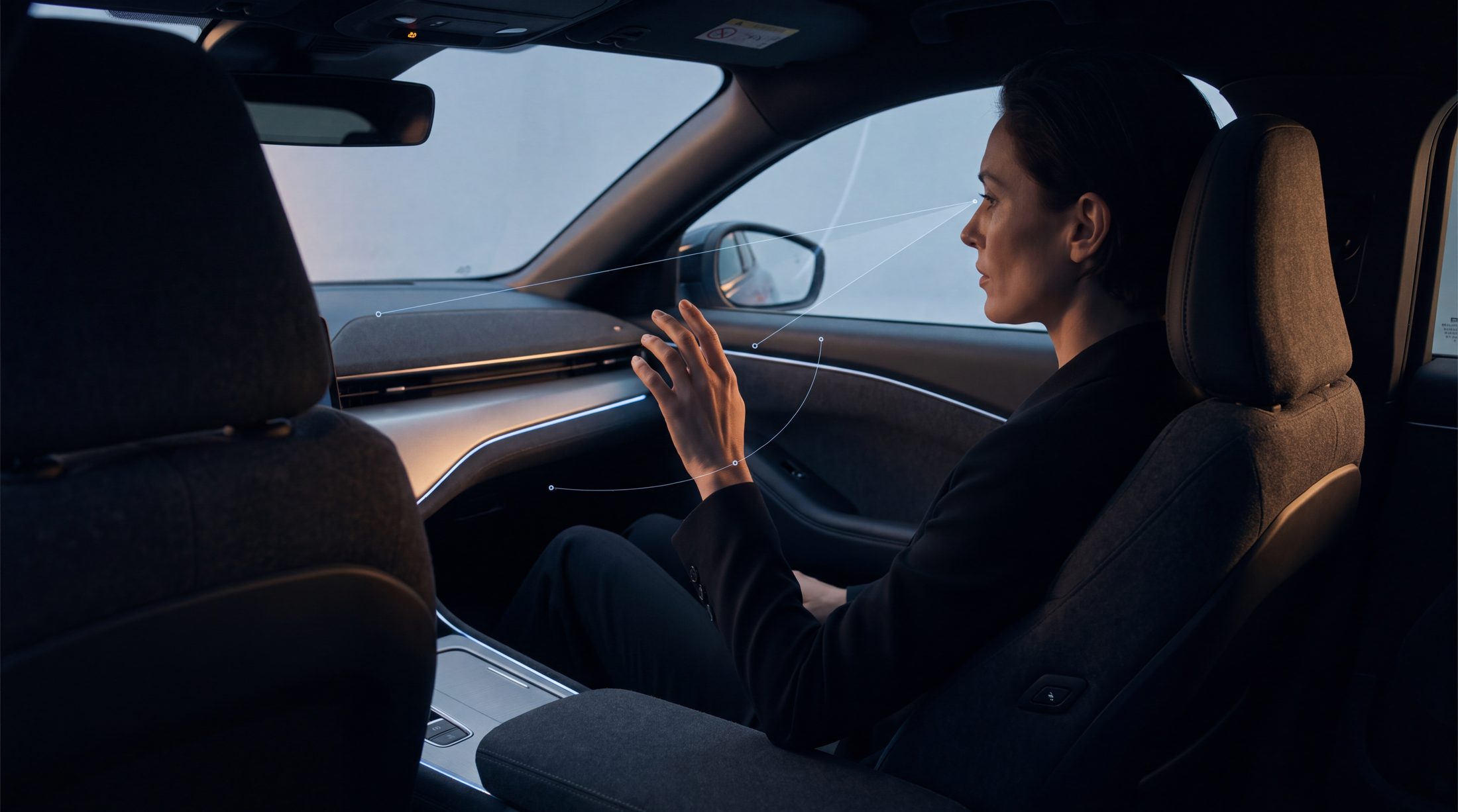A driver gesturing inside a premium vehicle cabin as the system anticipates the interaction